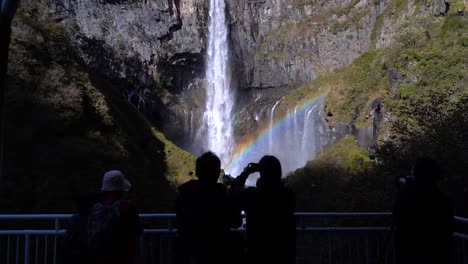 Empuje-En-Cámara-Lenta-Hacia-Las-Siluetas-De-Las-Personas-Que-Miran-La-Hermosa-Cascada-Alta-Con-Arco-Iris