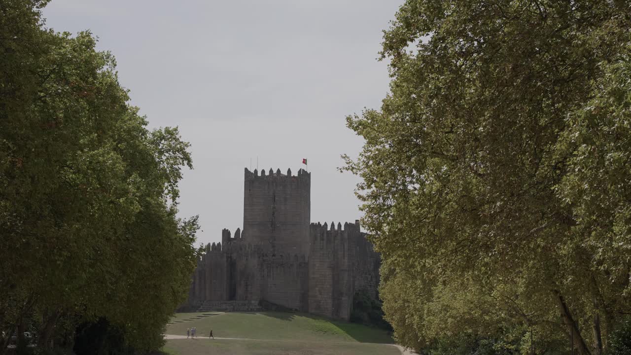 Castillo histórico de Guimarães enmarcado por exuberantes árboles verdes bajo un cielo brillante