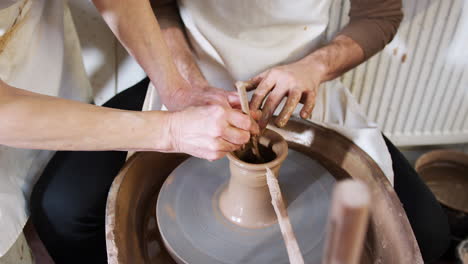 close up of male teacher helping man sitting at wheel in pottery class