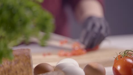 slow-motion of a chef slicing a red chili pepper on a wooden board. black gloves ensure hygiene, while a sharp knife cuts precisely. fresh ingredients tomatoes and herbs enhance the kitchen setting