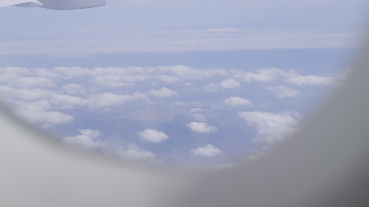 View from airplane window showing clouds and landscape below, passenger plane POV