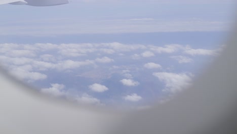 view from airplane window showing clouds and landscape below, passenger plane pov