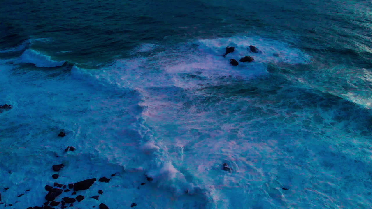 Drone flying over ocean waves and rocks in blue early sunrise light with dramatic sea texture
