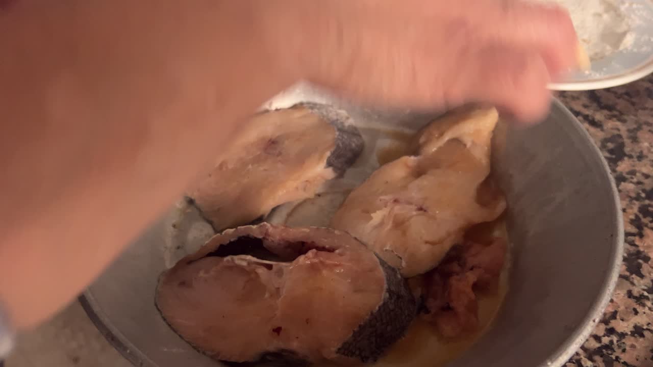 A person prepares fish fillets, adding cut slices to a metal plate, illustrating culinary skills and seafood preparation.