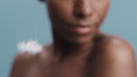 close up beauty portrait attractive african american woman feathers falling on smooth skin touching bare shoulders enjoying natural skincare gently caressing body in blue background slow motion