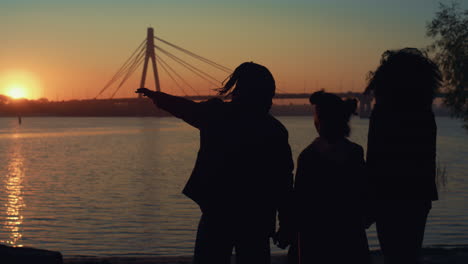 relaxed family silhouette standing on river shore. beautiful golden sunset time.