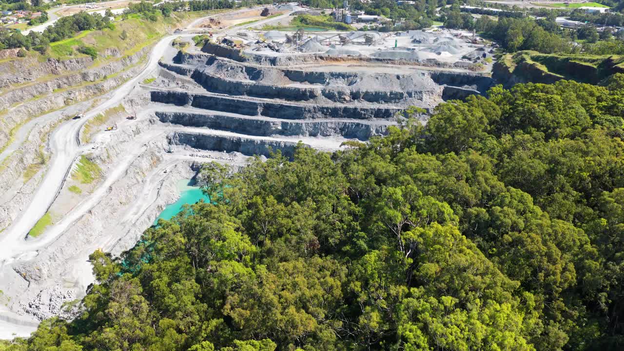 Aerial footage of a terraced quarry surrounded by lush greenery under bright daylight in Gold Coast, Australia