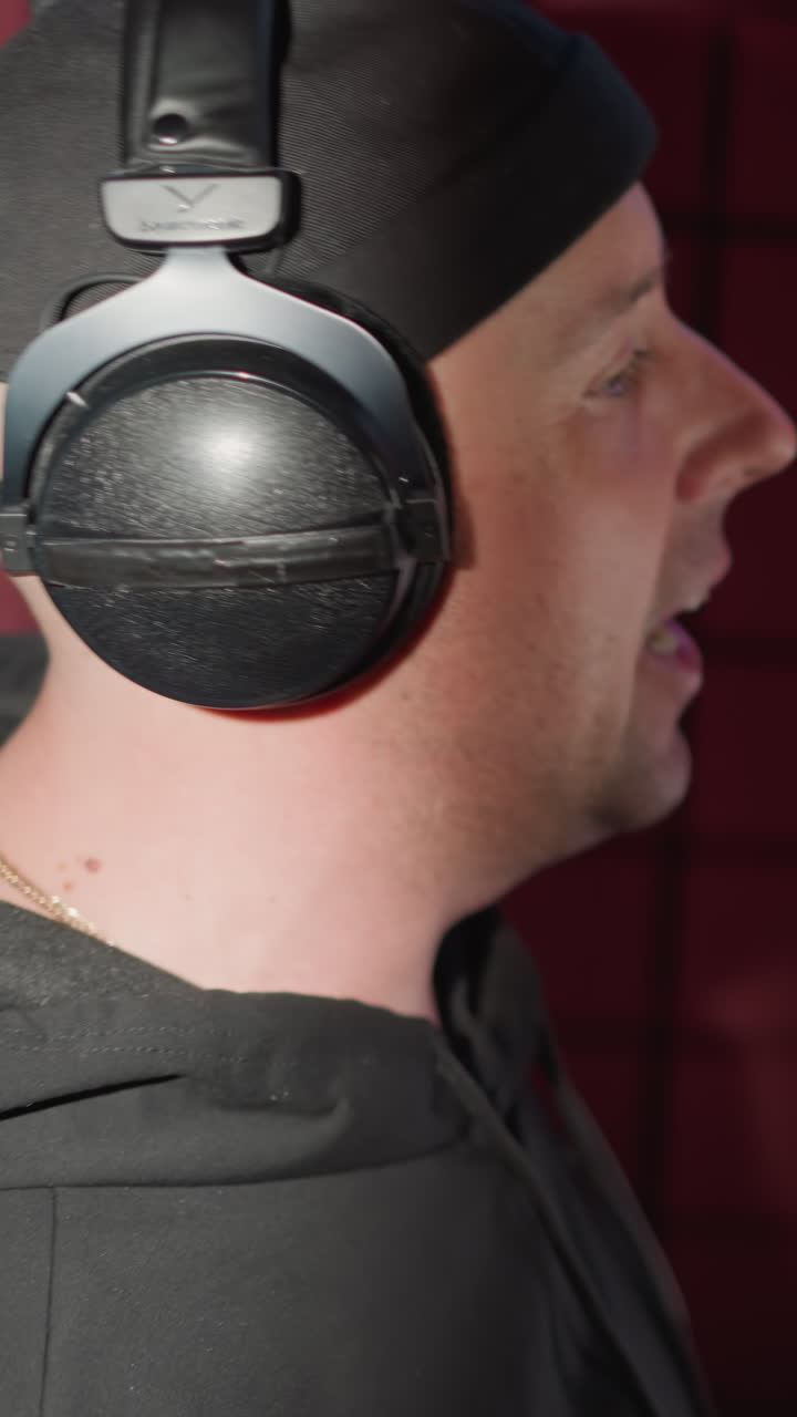 un hombre vestido de negro, cantando apasionadamente en un micrófono en una sala de grabación a prueba de sonido. el cantante lleva auriculares y hace movimientos expresivos de las manos, completamente inmerso en la música