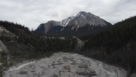 Aerial-overview-of-a-dried-creek-river-with-a-beautiful-mountain-rocky-peak-in-the-background-having-snow-on-top,-wide-shot,-conservation-concept,-flying-forward