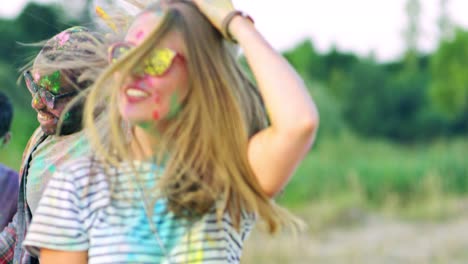 cute young pretty girl laughing, having fun and dancing among multiethnic friends in the field at the holi celebration