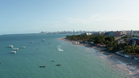 Camión-A-La-Derecha-Que-Sube-A-La-Derecha-Toma-Aérea-De-Drones-De-La-Playa-Tropical-Bessa-En-La-Ciudad-De-Joao-Pessoa,-Paraiba,-Brasil-Con-Gente-Disfrutando-Del-Océano,-Botes-Turísticos,-Motos-Acuáticas-Y-Rascacielos-En-El-Fondo