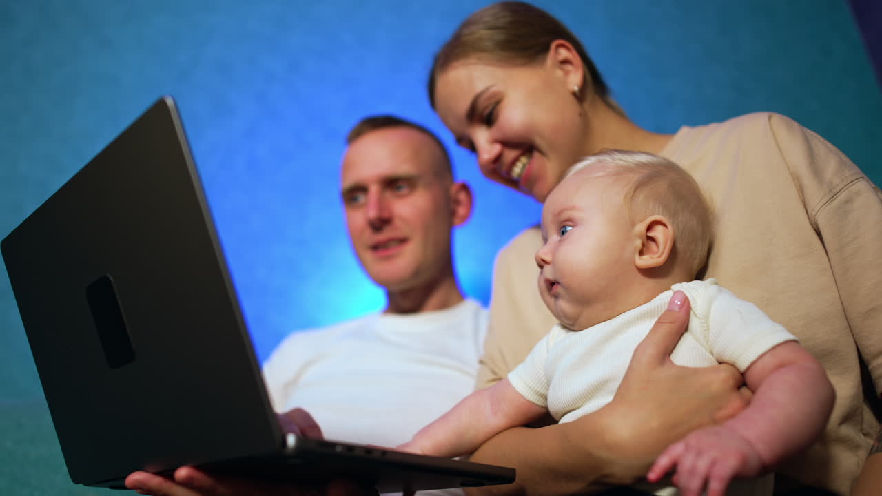 Family of three sitting in front of computer. Parents and a baby boy are focused on the screen. Low angle view.