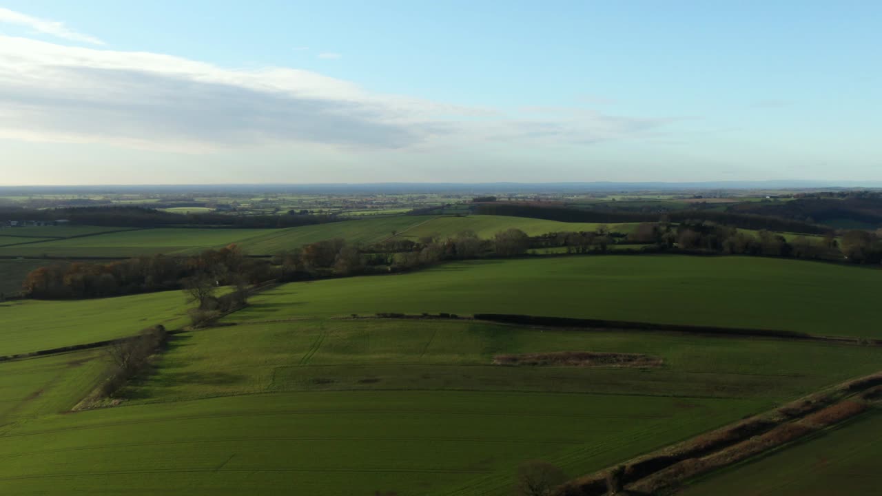 Drone flying cold winter green fields at high altitude and zoom creating parallax movement over gentle rolling hills in north yorkshire countryside in England and blue skies with some cloud