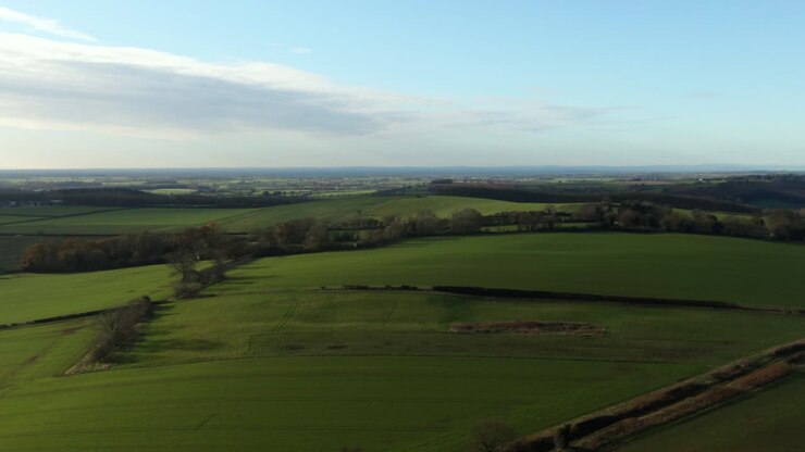 Drone flying cold winter green fields at high altitude and zoom creating parallax movement over gentle rolling hills in north yorkshire countryside in England and blue skies with some cloud