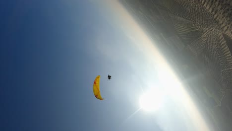 vertical format: aerial orbits below motor paraglider in blue sky