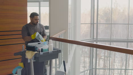 Arabic-Cleaning-Man-Holding-Rag-And-Cleaning-Product-While-Dancing-Near-A-Cleaning-Cart-Inside-An-Office-Building