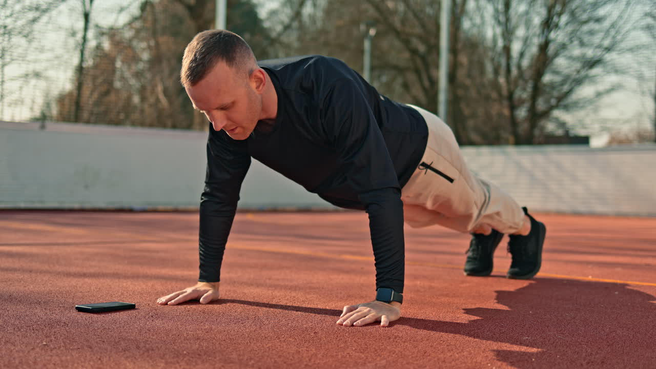 Un uomo sta facendo sport su un campo sportivo all'aperto. In estate, si dedica al proprio corpo svolgendo esercizi per la tonificazione e il miglioramento della forma fisica.