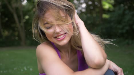 Pretty-young-blonde-woman-sitting-in-a-park-smiles-and-laughs-as-she-faces-the-camera