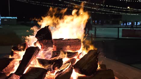 stationary slow motion close up of outdoor bonfire at night with people ice skating in the background