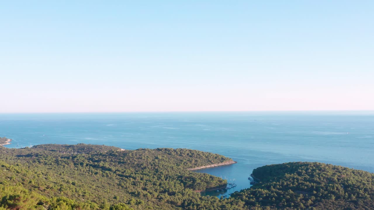 Carrellata aerea su una cresta boscosa che rivela la costa dell'isola di Lussino, Croazia, sottostante