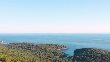 Dolly-Aéreo-Disparó-Sobre-Una-Cresta-Boscosa-Que-Revela-La-Costa-De-La-Isla-De-Losinj,-Croacia-Debajo