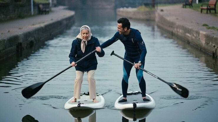 Young Man Teaching Elderly Woman to Stand Up Paddleboard on Canal