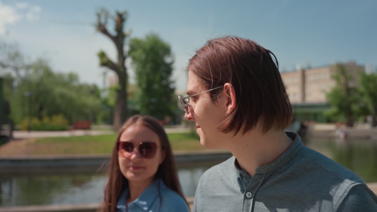 salida urbana informal, amigos caminando por la vía fluvial, dos compañeros conversan tranquilamente junto a la vista del canal, amigos vestidos de manera informal conversan amigablemente mientras caminan cerca del río