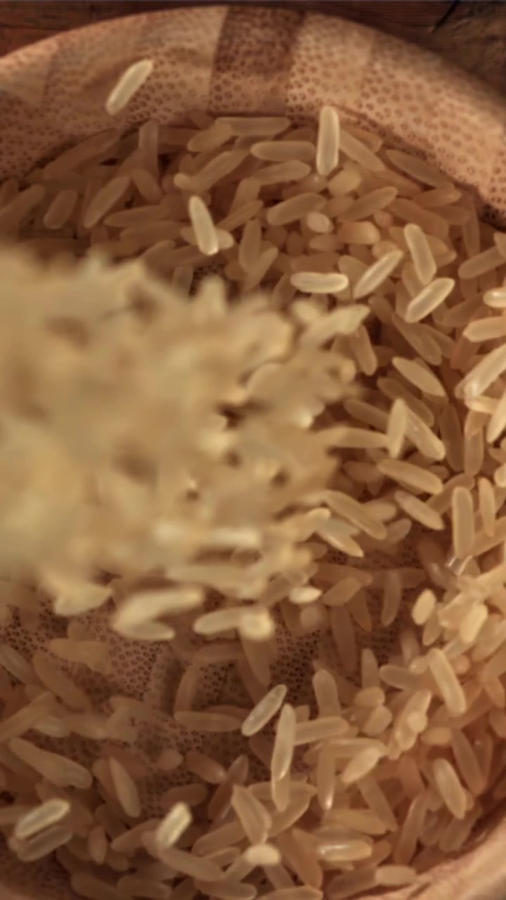 Chicchi di riso che cadono al rallentatore in una ciotola di legno
