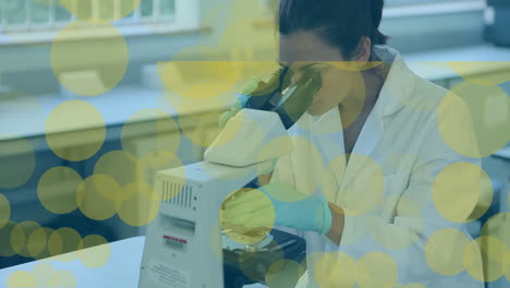 animación de puntos flotando sobre una trabajadora de laboratorio biracial usando un microscopio