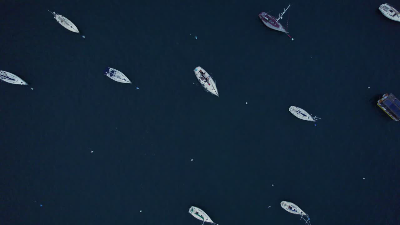 Overhead aerial view of small boats and yachts neatly spaced on deep blue water, creating a peaceful, geometric maritime scene.
