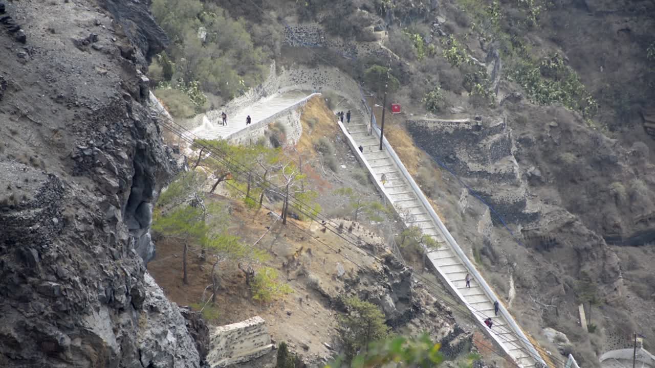 teleféricos bajando por la caldera en santorini, grecia, con turistas indistinguibles en una larga escalera