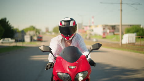 una motociclista monta una bicicleta eléctrica roja con su camisa abierta, revelando un singlet debajo, ella viaja sola a través de una ciudad, con edificios borrosos y coches visibles en el fondo