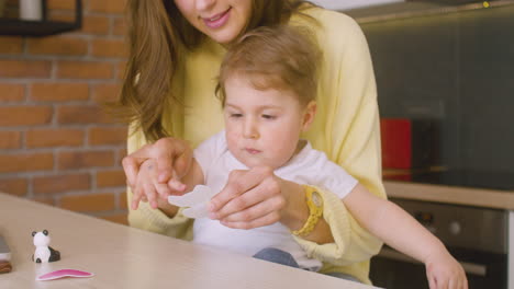 mujer sosteniendo a su hijo en su regazo mientras está sentada en la cocina y jugando con él con pegatinas de animales