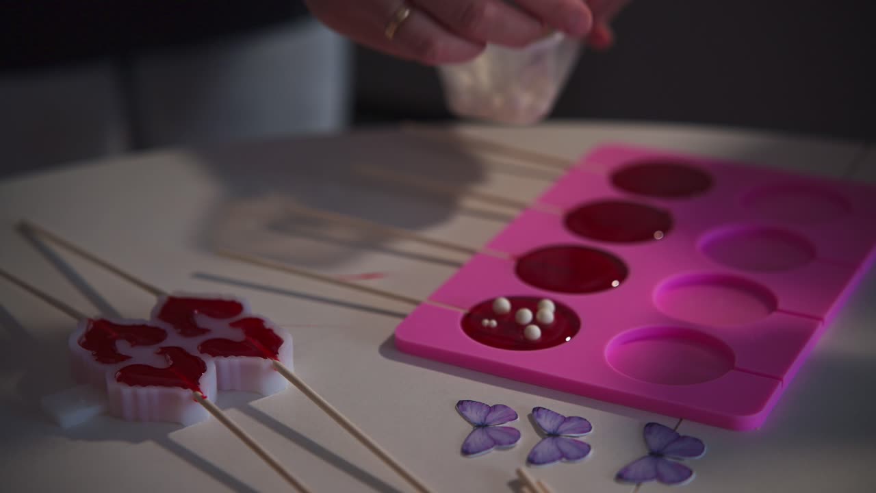 Primo piano di mani che decorano lecca-lecca rossi in uno stampo di silicone