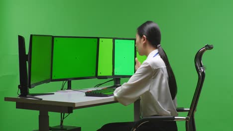 woman working at a multi-monitor desk in a green screen environment