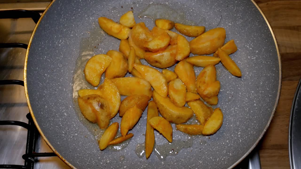 Potatoe quarters are being fryed in hot pan with hot and boiling oil on gas stove