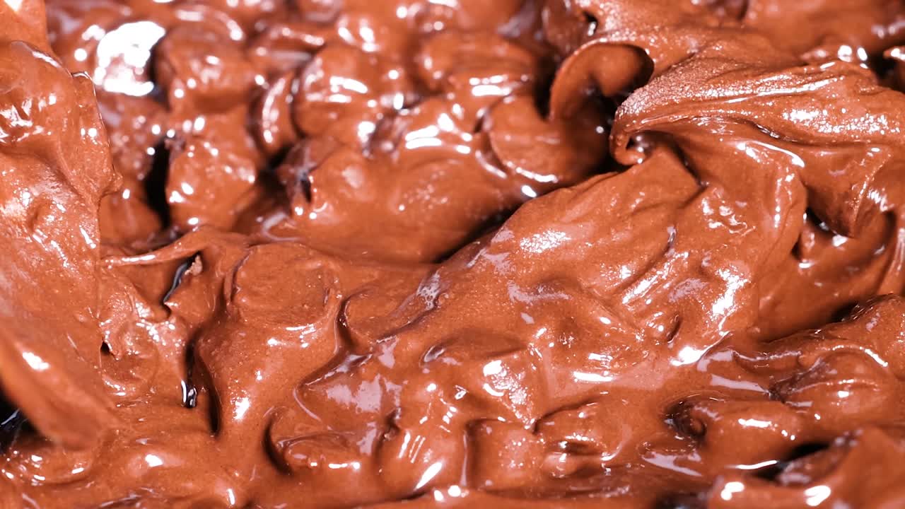 Close-up of a spoon stirring glossy, melted chocolate, creating a rich, smooth texture.