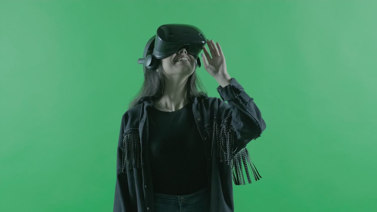 Giovane donna si guarda intorno e si meraviglia di quanto sia incredibile nel visore VR. Casco per la realtà virtuale su sfondo verde. Chroma Key.