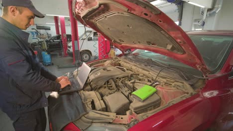 computer diagnostics of cars, young mechanic specialist male uses laptop technology while repairing vehicle with open hood at service station