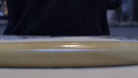 thin rolling pin being used to flatten out fresh dough on table