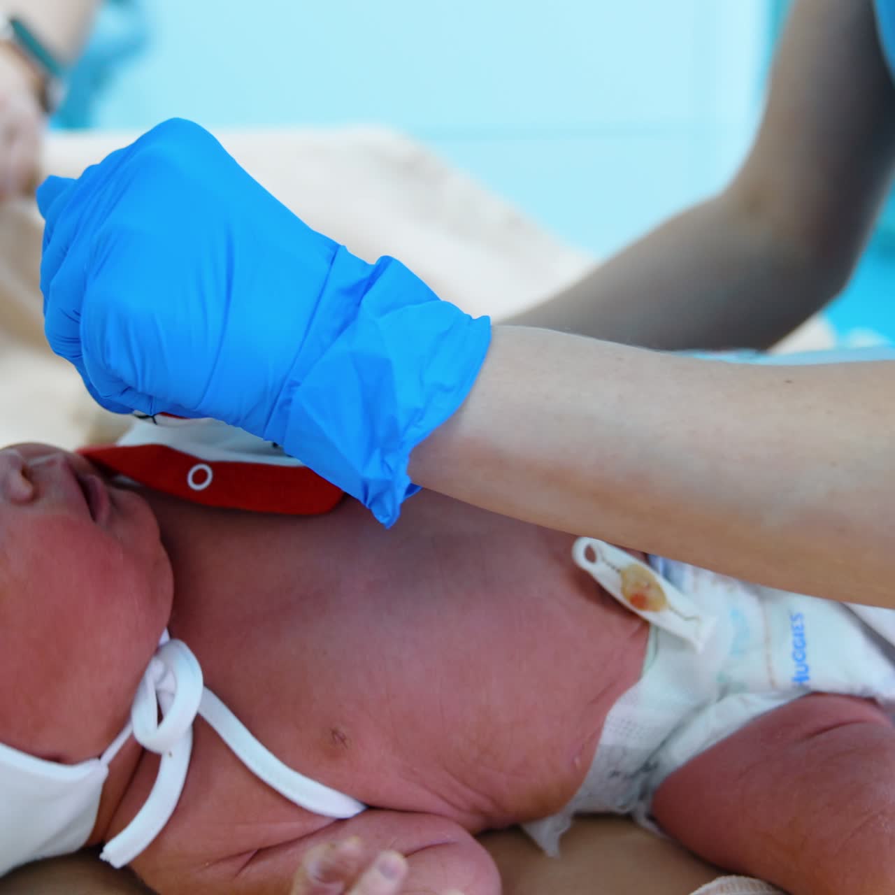Tiny newborn baby is dressed by the nurse. Child dislikes the process but doesn't cry. Side view close up