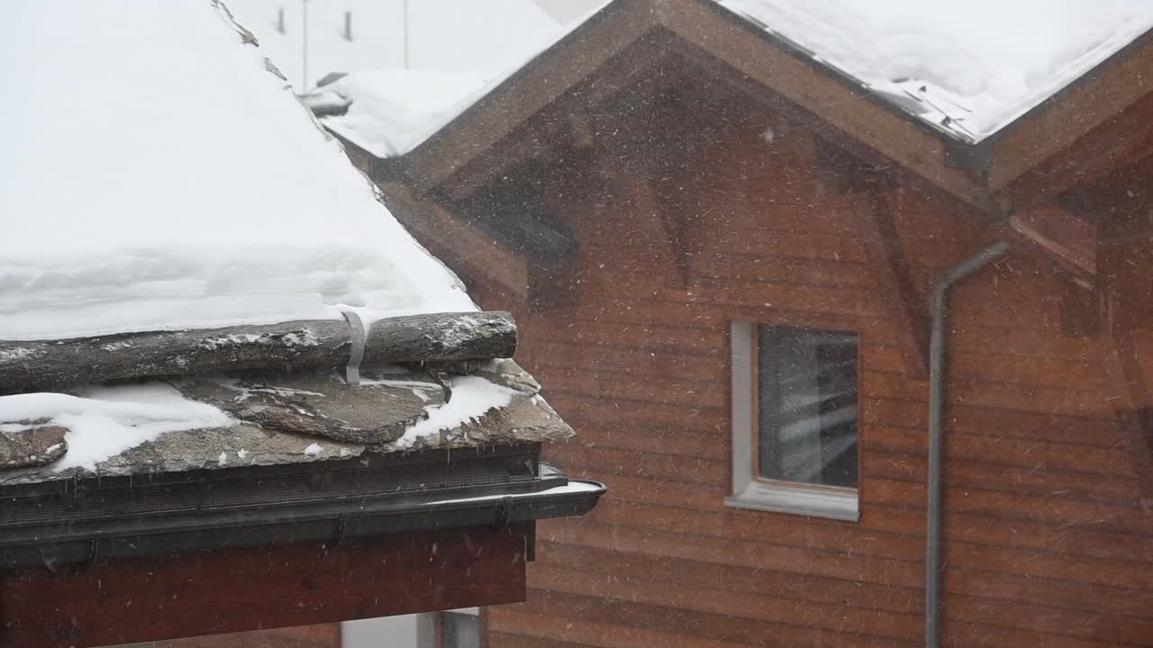 vista estática de un tejado y un canalón, con ráfagas de viento y partículas de nieve, pueblo suizo en invierno, alpes