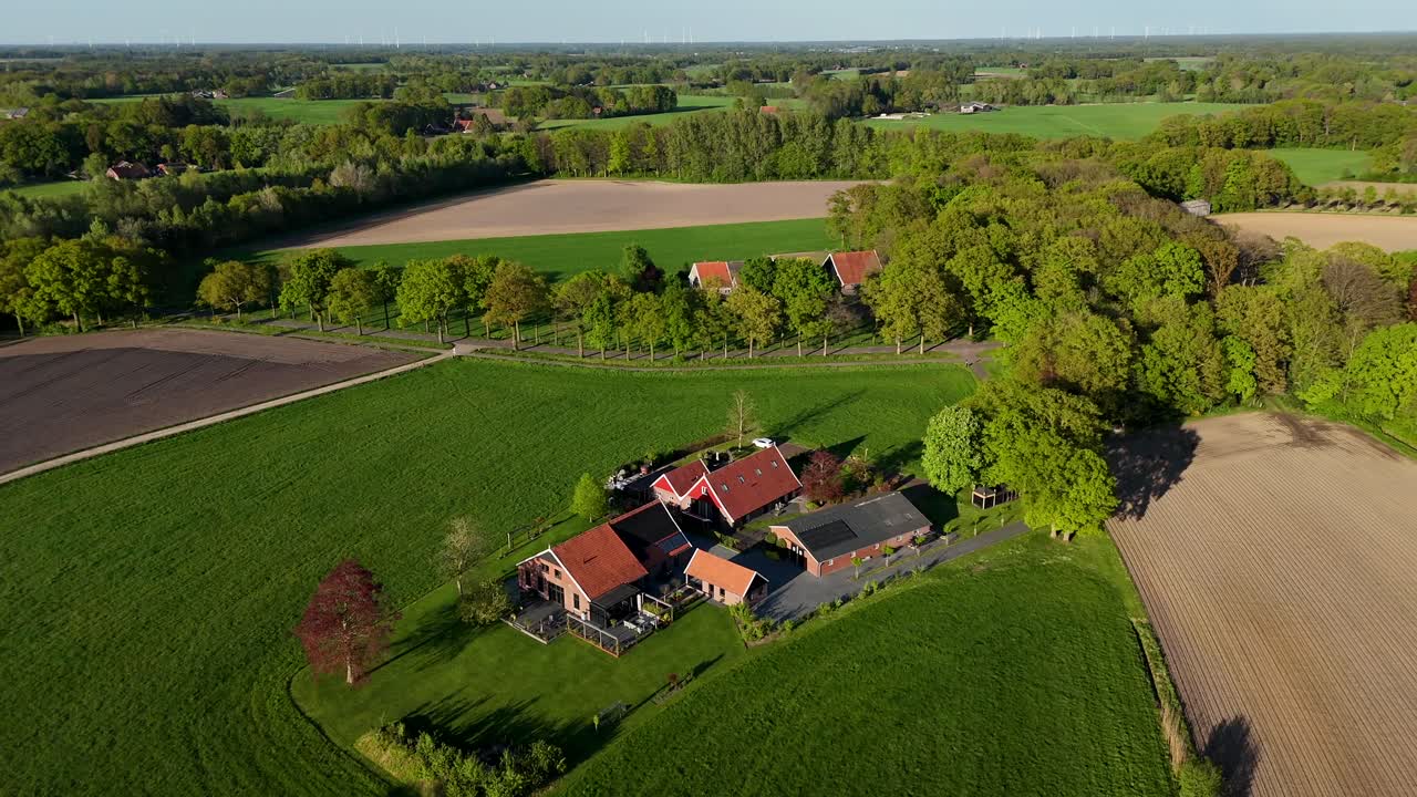 Rural idyllic farmers landscape in America during golden hour. Aerial orbit shot. Farmers House and Stable with modern solar panels on roof. Colored trees and fields in spring season. Quiet atmosphere