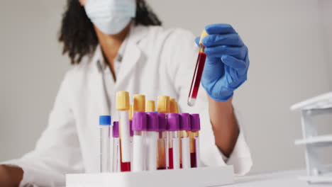 video of biracial female doctor with face mask holding test tube on blue background