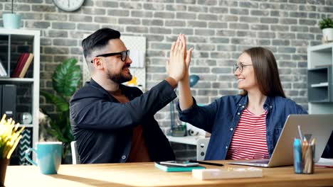 bucle de cinemagraph de colegas haciendo high-five sentado en la mesa en la oficina