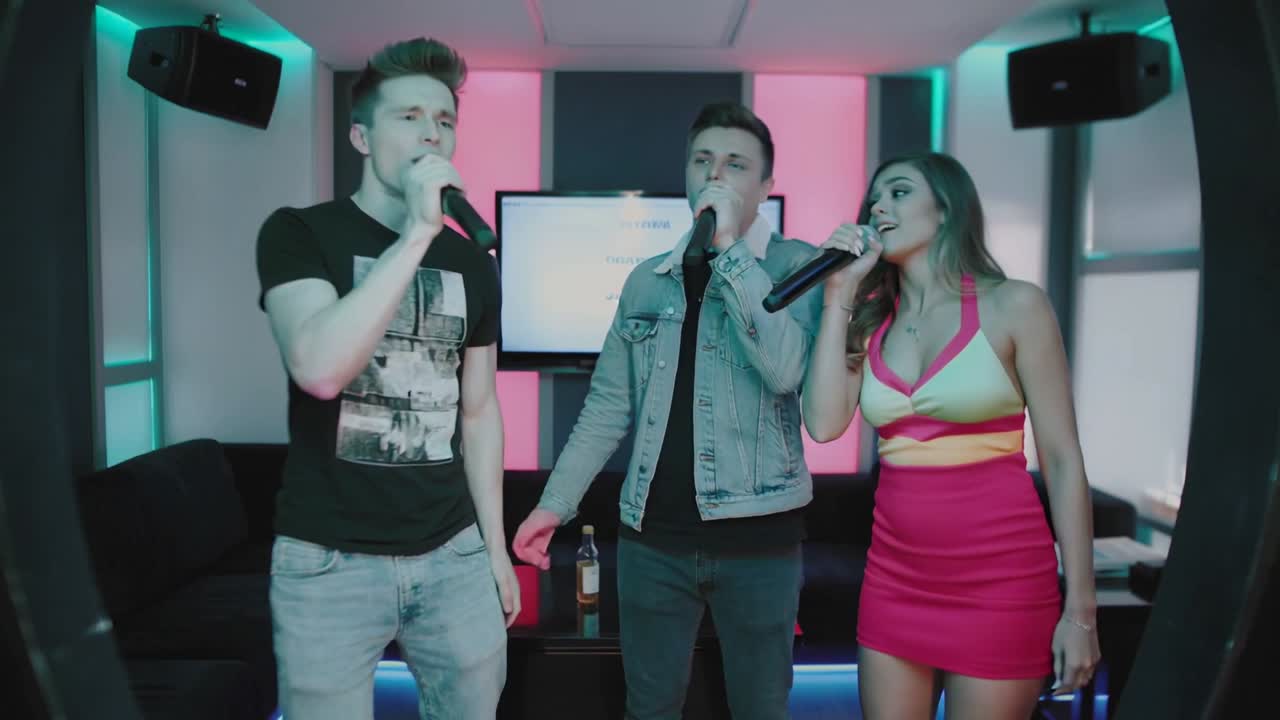 Following lyrics, three friends trading vocals and harmonizing in karaoke bar with mics