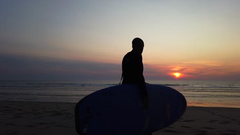 Silhouette-of-man-with-surfing-board,-walking-on-the-beach-against-beautiful-sunlight