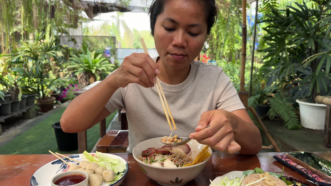 Asian Woman Eating Thai Noodles And Street Food Using Chopsticks and Soup Spoon At Eatery. medium shot