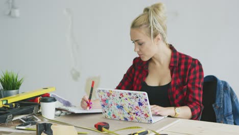 female with laptop writing in notebook