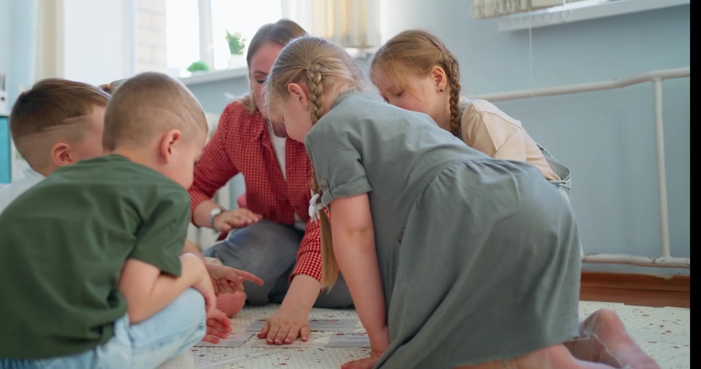 Lærer og små børn spiller læringskortspil på gulvet